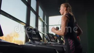 可爱的年轻女孩在健身房全景视窗前的跑步机上跑步。 带跑步机和大型健身房